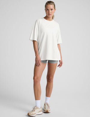 model wearing a white oversized cotton t-shirt and grey shorts against a plain background.