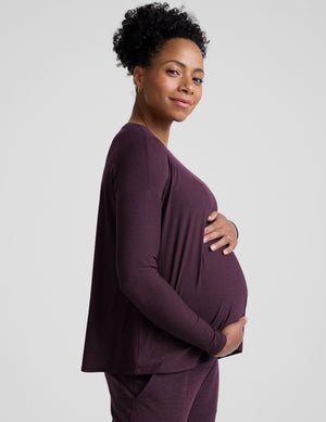 model wearing a purple maternity long sleeve crew neck top and joggers against a light gray background.