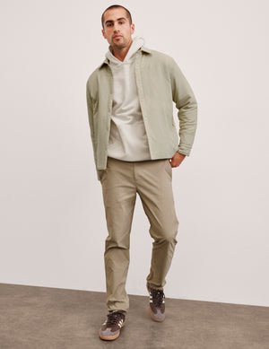 man wearing a light jacket and beige chino pants against a plain background.