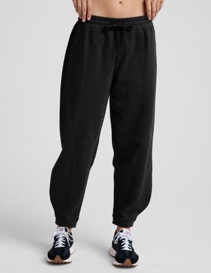 model is wearing black fleece barrel style sweatpants against a plain background.