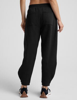 model is wearing black fleece barrel style sweatpants against a plain background.