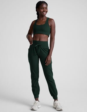 model wearing a green sports bra and green midi length joggers with a drawcord at the waistband against a plain background.