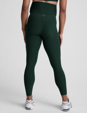 pregnant woman wearing green maternity leggings on a plain background.