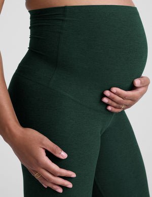 pregnant woman wearing green maternity leggings on a plain background.