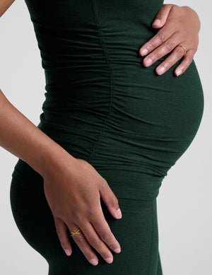 pregnant model wearing green maternity racerback tank top and green maternity leggings on a plain background.